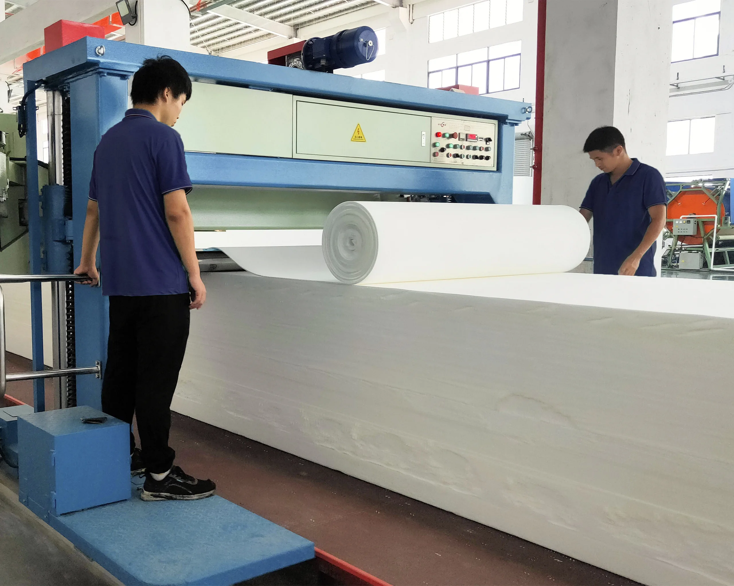 Workers operating machine to slice large foam blocks into uniform layers for mattress production, demonstrating efficient large-scale processing capability